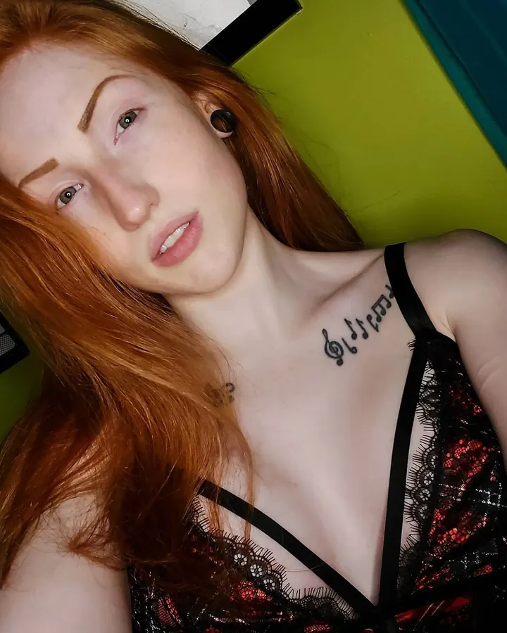 Femme aux cheveux roux, regard intense, portant des gants transparents noirs, en gros plan sur fond blanc.