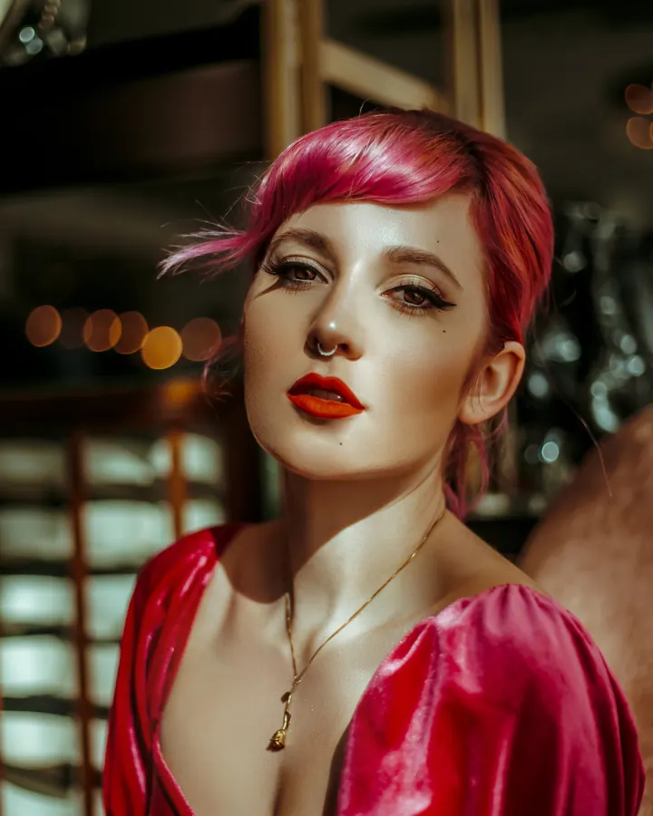 Femme asiatique aux cheveux roux, portant un haut blanc, posant devant un mur extérieur, main dans les cheveux