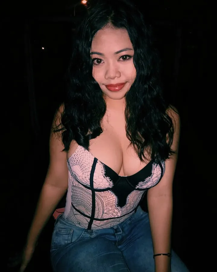 Femme aux cheveux noirs, portant un haut noir et un sous-vêtement blanc, allongée sur un lit, main dans les cheveux.