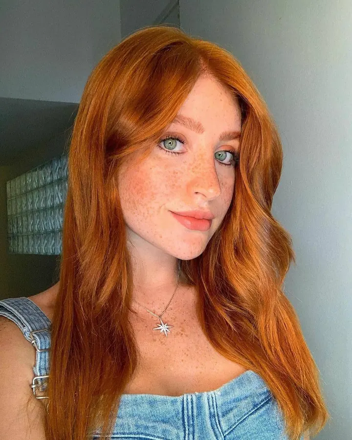 Jeune femme aux cheveux roux, regardant vers la caméra, portant une tenue décontractée bleue avec un collier étoile